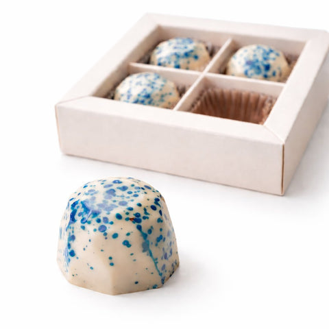 Einzelne handgemachte Pina Colada Eierpunsch-Praline vor 4er Geschenkbox – exklusives Alkohol-Konfekt aus weißer Schokolade als Sommergeschenk